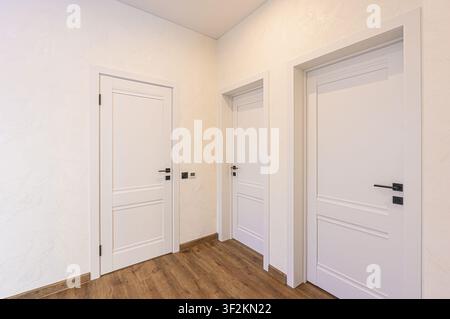 Interior shot featuring three white paneled doors with black handles against textured walls and wood-look flooring Stock Photo