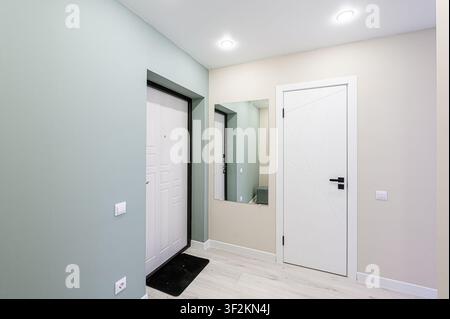 modern hallway featuring two white doors, a mirror, and pale walls. The color palette is light and airy, with minimalist design elements Stock Photo