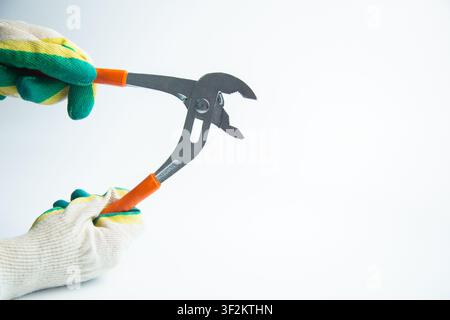 Two hands wearing protective gloves (green and yellow) hold adjustable pincers with bright orange Stock Photo