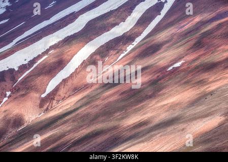 Diagonal patterns of red mountain slopes and melting snow create a dramatic natural abstract on Mount Kyzylnura, Uzbekistan. Stock Photo