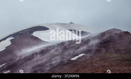 Cloud shadows sweep across the colorful slopes of Mount Kyzylnura, highlighting rugged ridges and lingering snow in a dramatic alpine panorama. Stock Photo