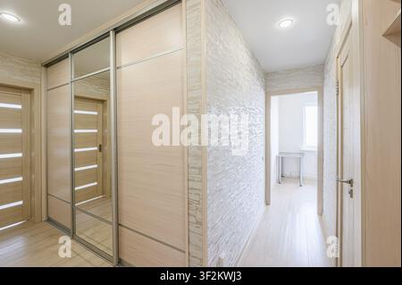well-lit hallway featuring a sliding door wardrobe with mirrored panels, textured wallpaper, and light wood flooring Stock Photo