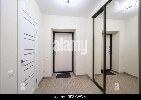 clean, modern hallway featuring three doors, a sliding mirror closet, and light wood flooring. Minimalist decor creates a bright, spacious feel Stock Photo