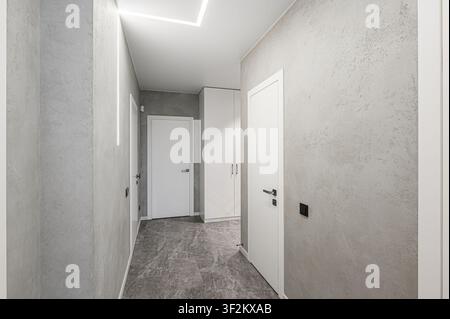 modern hallway with gray textured walls, white doors, and geometric lighting. The floor is gray marble tile Stock Photo
