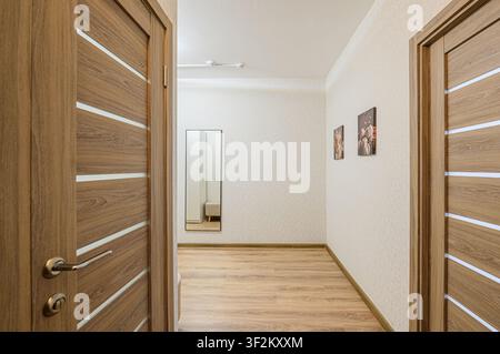 Hallway view with wooden doors, light patterned wallpaper, wooden floor, mirror, and pictures on the wall Stock Photo