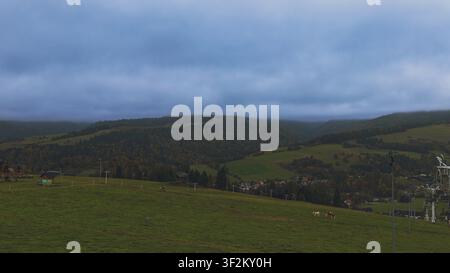 cenic view of mountain slopes covered with autumn forest and green pastures under heavy overcast sky. Quiet rural valley landscape with dramatic cloud Stock Photo