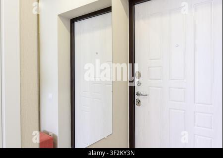 Hallway with two white panel doors framed in dark trim. One door is a mirror reflection. Walls are light beige Stock Photo