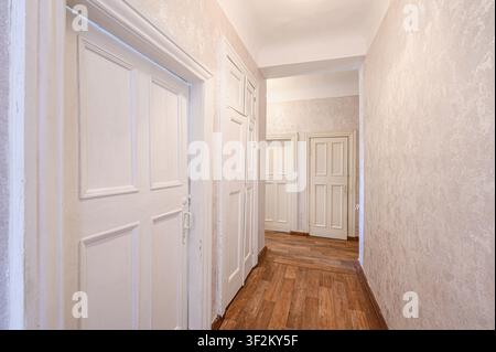 bright hallway with white paneled doors and textured light beige walls. A wood-like floor runs the length, leading to additional doors in the distance Stock Photo