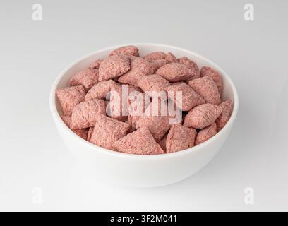 Fruit pillows, strawberry corn pads for breakfast in bowl. Pink crispy corn flakes with milk and berry filling on white background Stock Photo