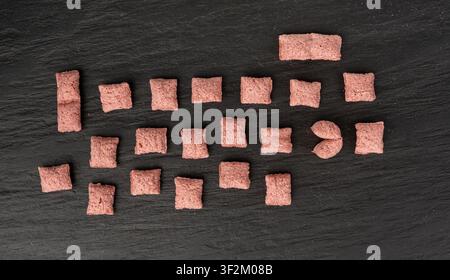 Fruit pillows, strawberry corn pads for breakfast. Pink crispy corn flakes with milk and berry filling on black stone background top view Stock Photo