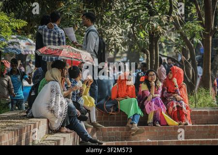 Dhaka, Bangladesh - February 27, 2017: A group of young adults, some holding papers and umbrellas, sit and stand on reddish-brown brick steps under a Stock Photo