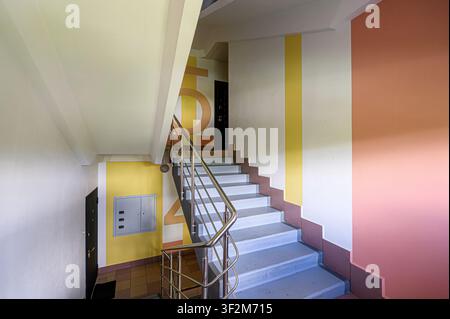 stairwell in an apartment building, featuring a metal railing, pastel-colored walls, and a staircase leading upwards Stock Photo