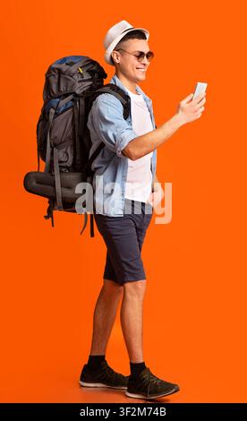 Hiker using trekking app on mobile phone over orange background Stock Photo