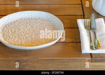 Empty ceramic restaurant plate on wooden table with folded napkin and cutlery prepared for elegant dining service. Stock Photo