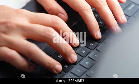 Close-up of female hands typing on a sleek black laptop keyboard during remote work or study. Stock Photo