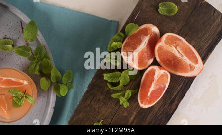 Juicy grapefruit slices are arranged on a rustic cutting board with fresh mint leaves and an orange citrus drink. Soft natural side lighting brings ou Stock Photo