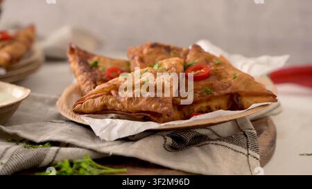 Golden-brown triangular pastries rest on parchment paper inside a rustic plate. Bright natural light emphasizes the blistered, crunchy textures of the Stock Photo