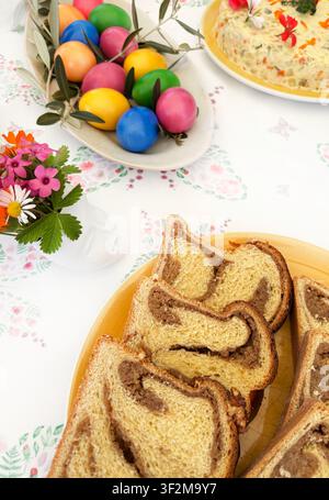 Slices of traditional Romanian Cozonac sweet bread with walnut cocoa filling, on a festive table setting with colorful painted Easter eggs. Stock Photo