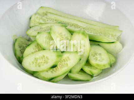 Cucumber cuts and slices in white bowl close up. Green vegetable cuts for salad isolated, healthy natural plant pieces, macro cucumbers slicing on whi Stock Photo