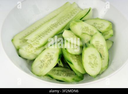 Cucumber cuts and slices in white bowl close up. Green vegetable cuts for salad isolated, healthy natural plant pieces, macro cucumbers slicing on whi Stock Photo