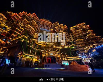 5 November 2025, Zhangjiajie, Hunan, China - Illuminated Tujia-style multi-story complex with traditional curved roofs and laser light show at night in Zhangjiajie. Stock Photo