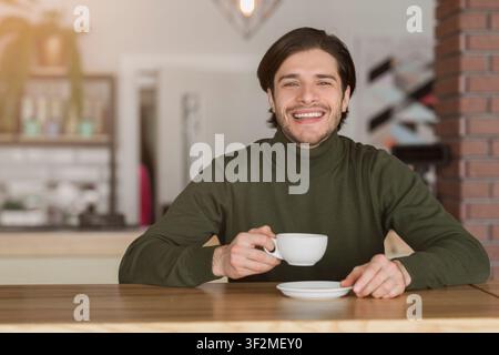 Young cheerful man drinking tea or coffee at cafe Stock Photo