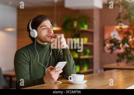 Pensive guy in headphones listening to music, using smartphone Stock Photo