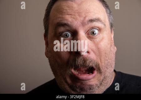Man with short hair and dark shirt looks surprised Stock Photo