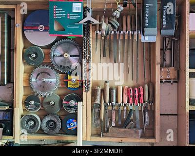 Organized woodworking and metalworking tools on a workshop wall. Circular saw blades, files, chisels, abrasive discs and hand tools neatly arranged in Stock Photo