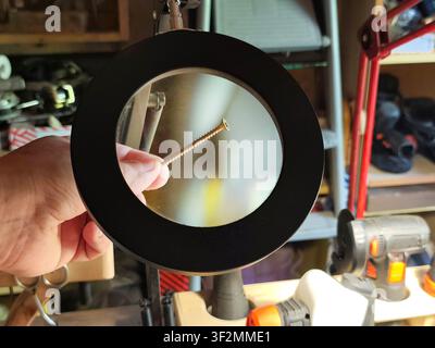 Magnifying glass inspecting a wood screw in a workshop. Close-up of hardware under magnification, concept of precision, quality control, repair, craft Stock Photo