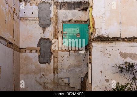 Partially demolished wall exposing weathered masonry and surviving green ceramic tiles, illustrating urban decay, renovation and architectural change. Stock Photo
