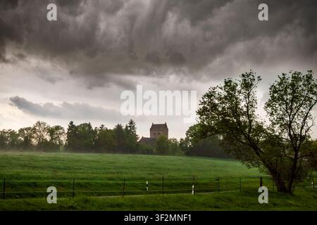 Dark storm clouds gather above a rural church and farmland in Brandenburg as rain falls across the agricultural landscape Stock Photo