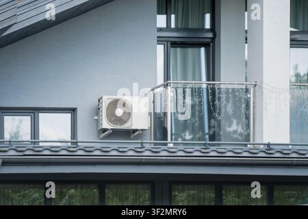 Outdoor air conditioner compressor unit installed on a residential house wall next to a modern balcony representing HVAC appliance setup Stock Photo