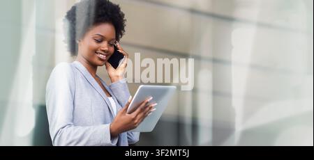 Smiling Black Woman Talking On Phone While Using Tablet In Modern Office, Business Concept Stock Photo