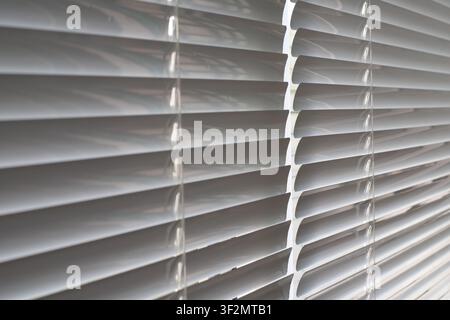 Close up background of dusty white metal venetian blinds. Horizontal window slats with cord thread slots covered in dust layers inside office or apart Stock Photo