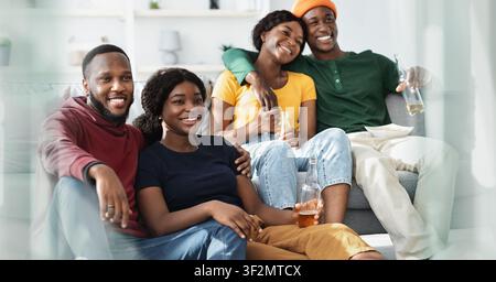 Happy Young Multiracial Group Enjoying Drinks At Home, Relaxing On Couch Together Stock Photo