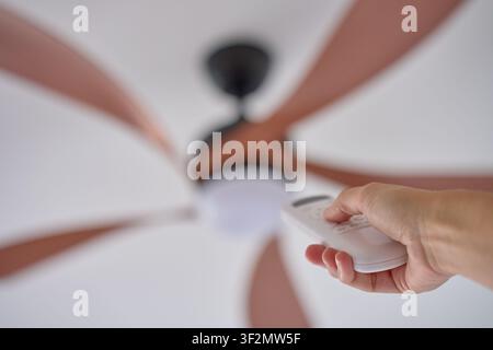 Person using remote control to operate ceiling fan mounted on white ceiling. Concept of indoor comfort and modern household technology Stock Photo
