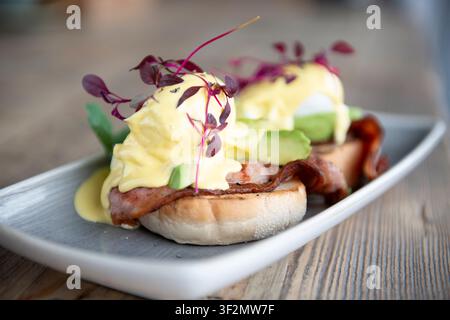 Delicious Eggs Benedict Served With Fresh Greens and Herbs on a Wooden Table Stock Photo
