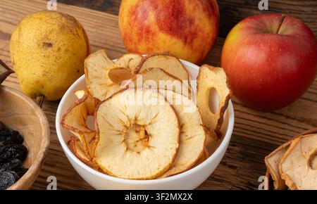 Dry apple slices on wood table. Dried apple chips, healthy fruit snack in bowl, dehydrated gourmet rings, crunch pitted sweet pear chips on rustic bac Stock Photo
