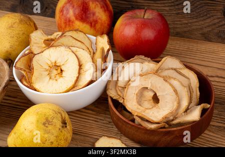 Dry apple slices on wood table. Dried apple chips, healthy fruit snack in bowl, dehydrated gourmet rings, crunch pitted sweet pear chips on rustic bac Stock Photo