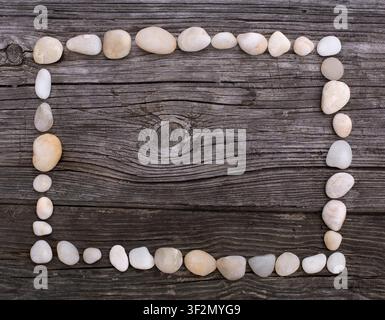 A rectangular frame of smooth white pebbles rests on a rustic weathered wooden surface. Stock Photo