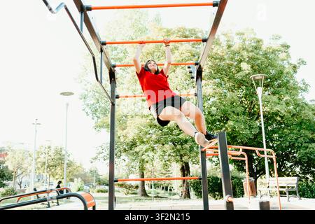 Young woman hanging from monkey bars during outdoor calisthenics workout Stock Photo