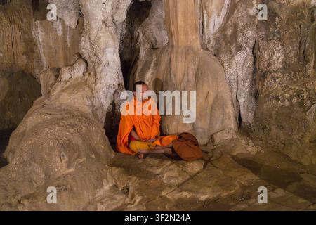 Buddhist monk meditating by stalegmites, in Tham Chang Cave, Vang Vieng, Laos Stock Photo