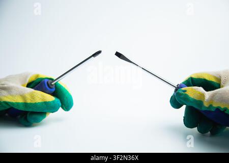 Close-up of two hands in work gloves holding screwdrivers against a white background. Concept of Stock Photo