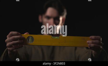 Hands holding a yellow spirit level in dramatic low light Stock Photo