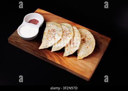 Studio high-angle shot of four golden folded pastries sprinkled with spices, served with dual dipping sauces in a white bowl on a rustic wooden board Stock Photo