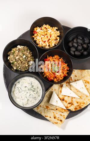 Studio overhead shot of assorted mezze appetizers including eggplant caviar, rice salad, olives, tomato dip, and yogurt sauce served in black bowls wi Stock Photo