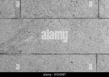 Close-up of a gray granite stone wall showing horizontal concrete tiles, subtle weathering and grainy surface detail. Ideal as an architectural backgr Stock Photo
