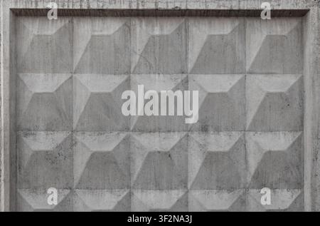 Weathered concrete fence block featuring repeating textured geometric relief pattern in monochrome. Urban architectural facade shows stains, decay and Stock Photo