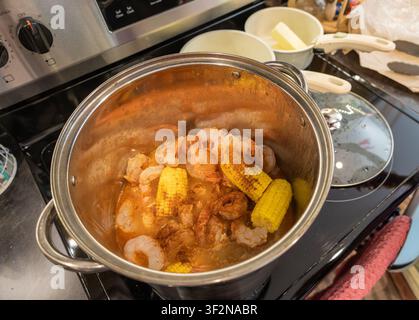 Shrimp and corn simmer in a pot on a stovetop. Rich, flavorful ingredients bubble gently. This close-up captures home cooking warmth and care. Ideal f Stock Photo